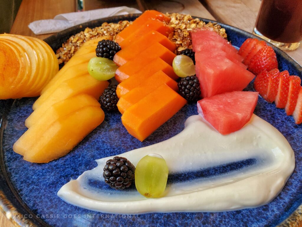 plate of cut fruit with a smear of yoghurt and a dash of muesli