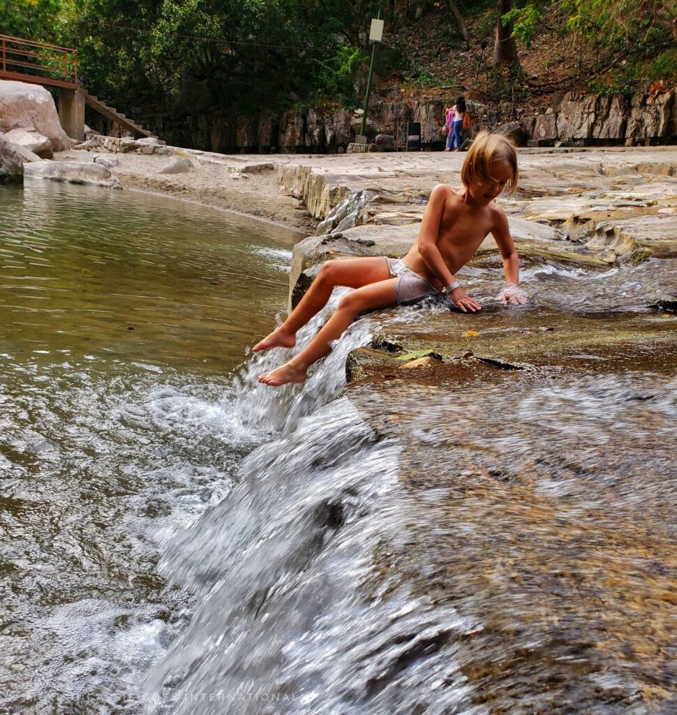 child sitting in water at a small waterfall