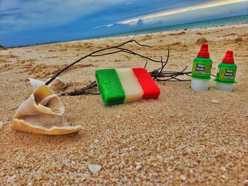 beach shot - small green, white, red (flag style) coconut candy on sand, two pelon pelo rico next to it