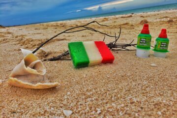 beach shot - small green, white, red (flag style) coconut candy on sand, two pelon pelo rico next to it