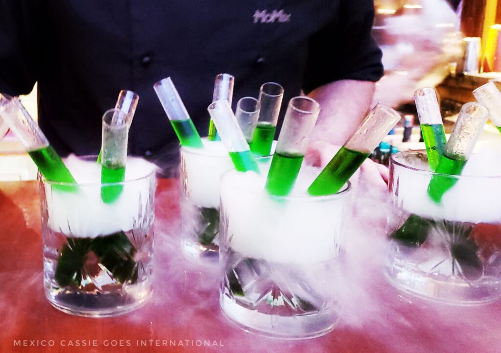  test tubes with green liquid in them in glasses. dry ice around