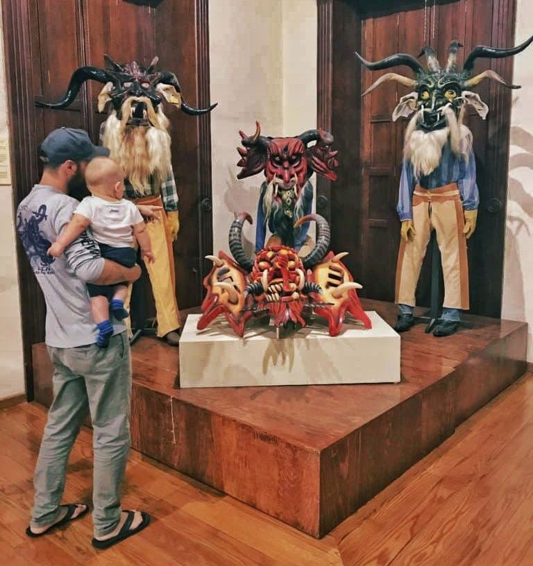 man and baby looking at a museum display of masks