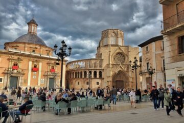 Valencia cathedral with people sitting at tables on the plaza in front. heavy grey sky.