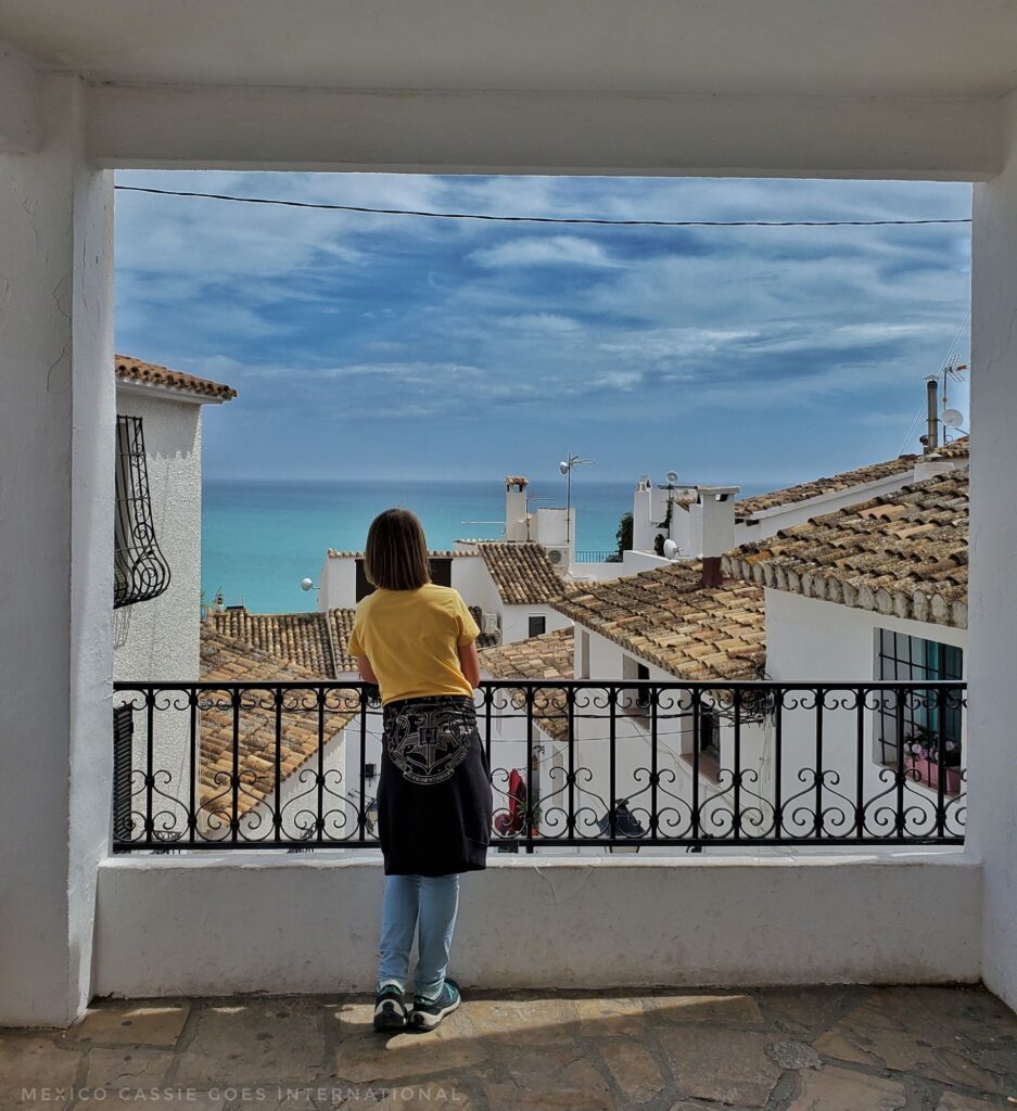 child standing leaning on a railing looking out over white houses to the ocean