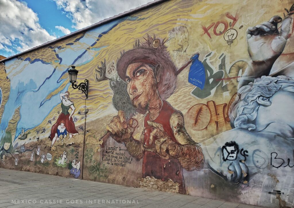 murals on a wall- main one is of a person from the waist up. wearing hat and carrying a hoe