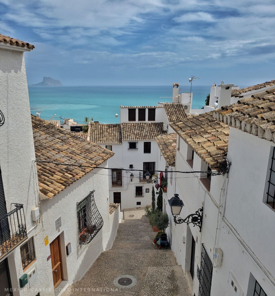 white houses on either side of road and at end of road, cobbled street, blue sea behind