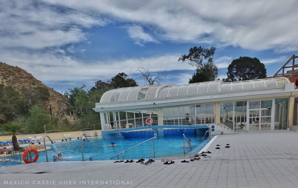 greenhouse style building behind a very blue pool - flipflops around edge, blue sky