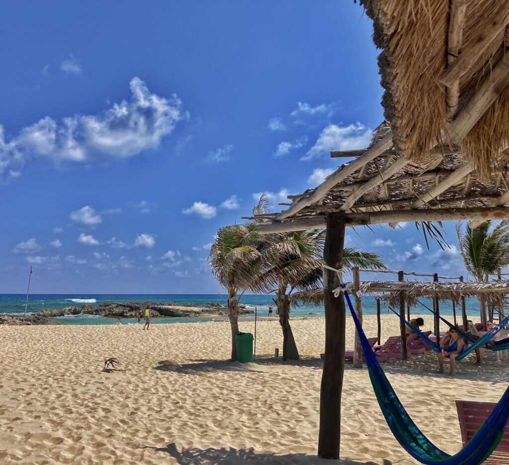 sandy beach, blue sea, hammocks under thatch roofs