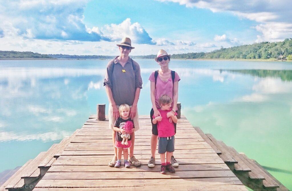 two adults and 2 small children standing on wooden pier surrounded by  still water. 