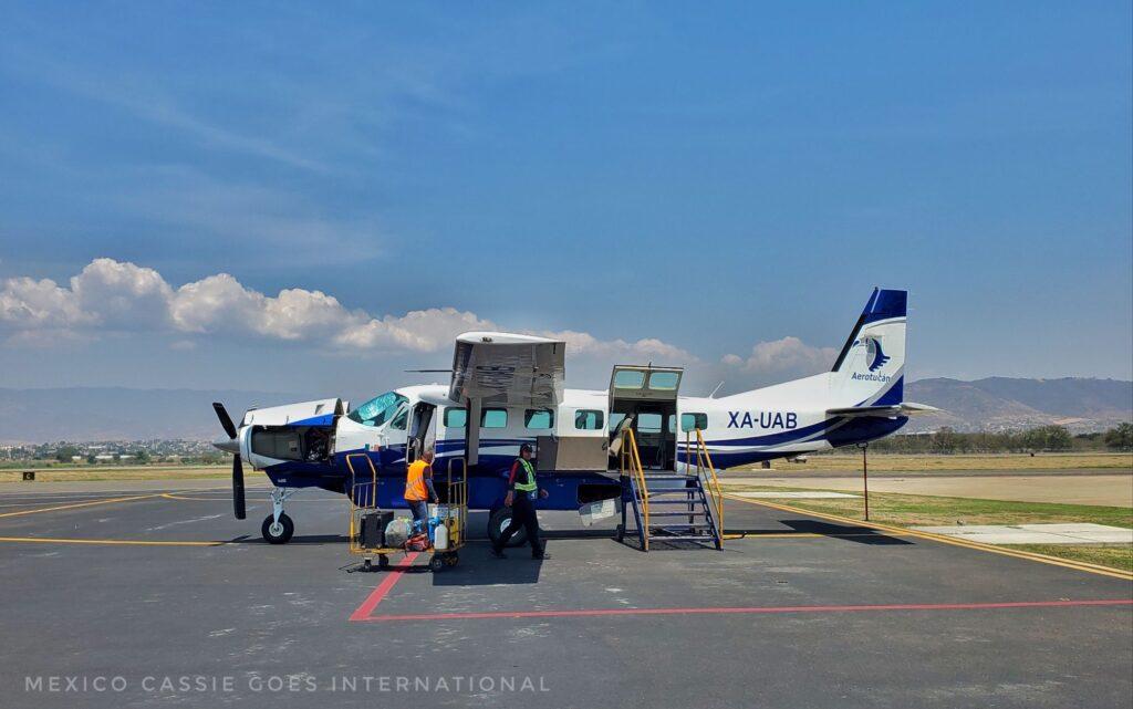 tiny plane (12 seater) with small ladder at back and ground staff sorting out luggage