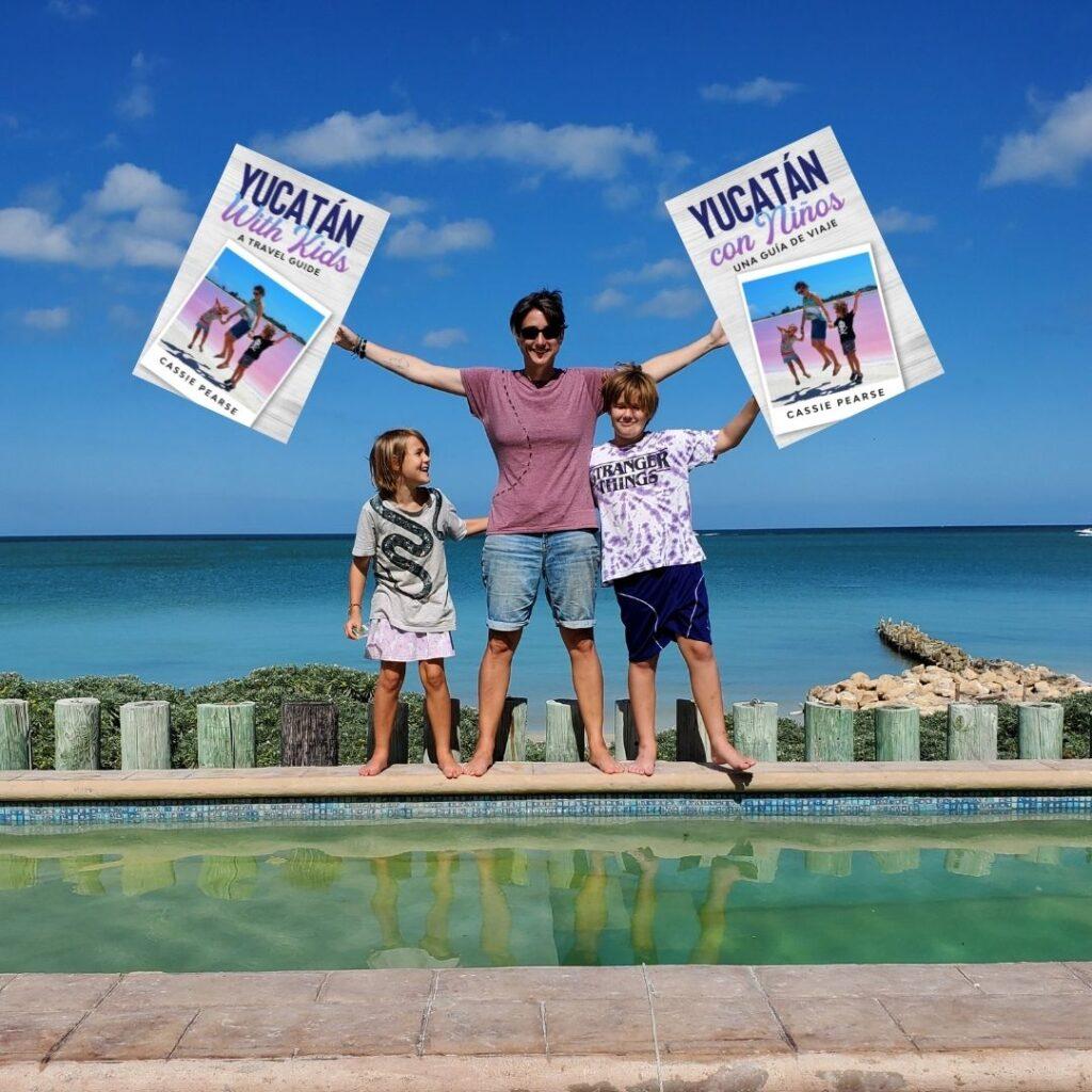 Adult standing with 2 kids, one on either side. Adult has arms outstretched and is holding a copy of an oversized book in each hand