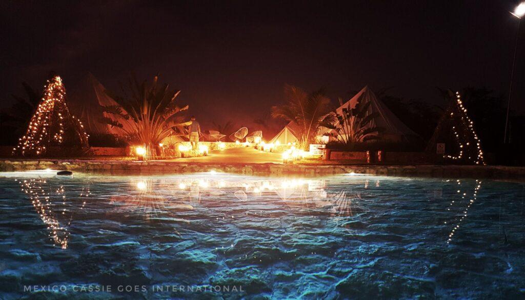 night scene of swimming pool, fire pit and tents