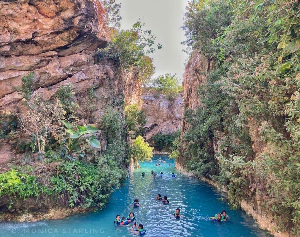 people swimming in blue water between 2 cliff sides