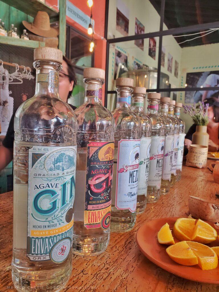 bottles of mezcal in a line - plate with cut up oranges in front