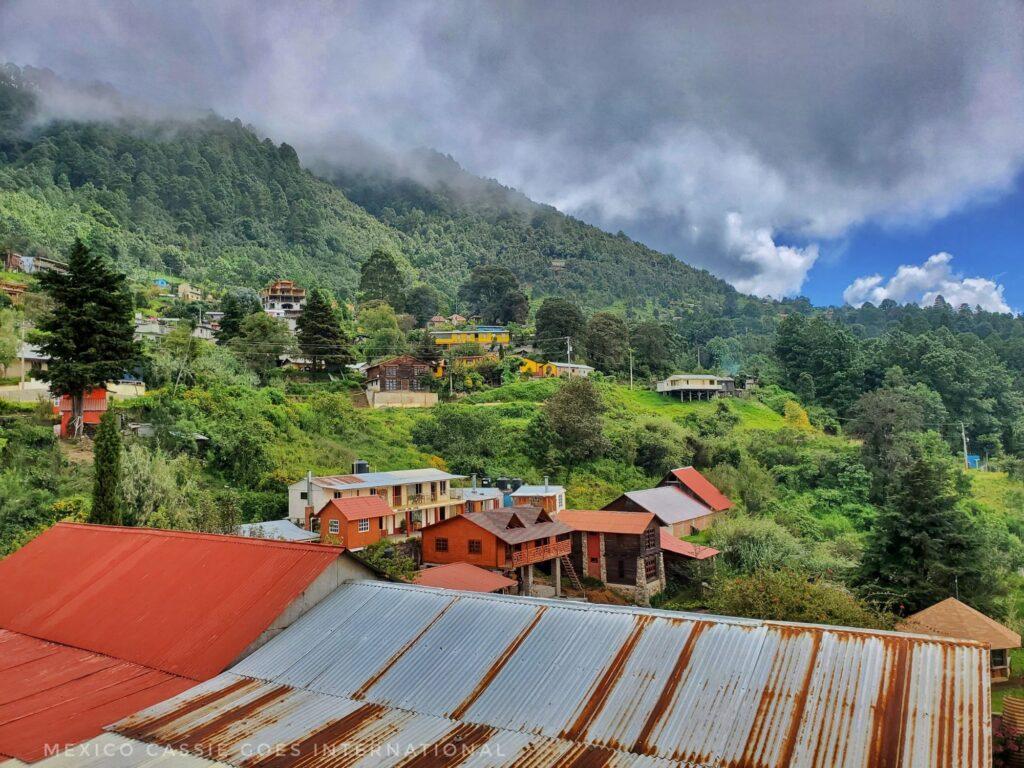 view over a tin roof to small group of houses, green trees on mountains, thin grey cloud