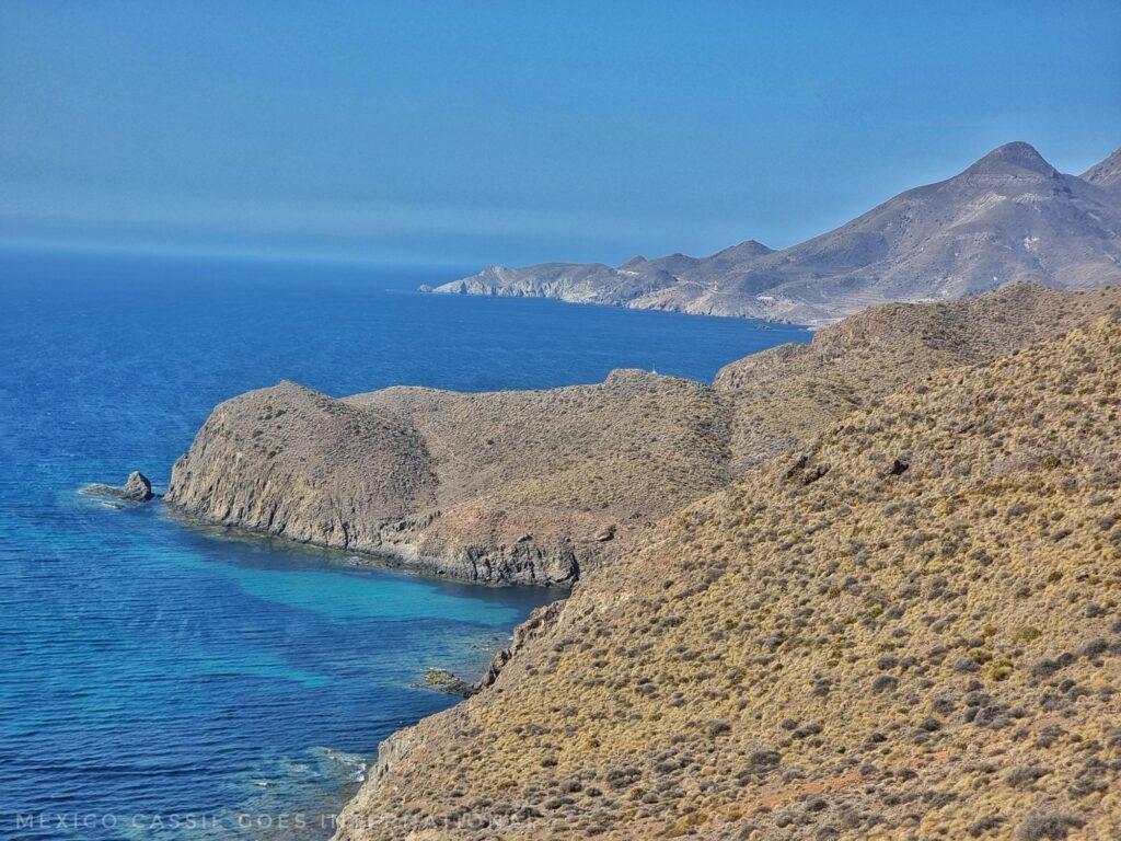 view along a coastline - v blue sea and mountains down to water