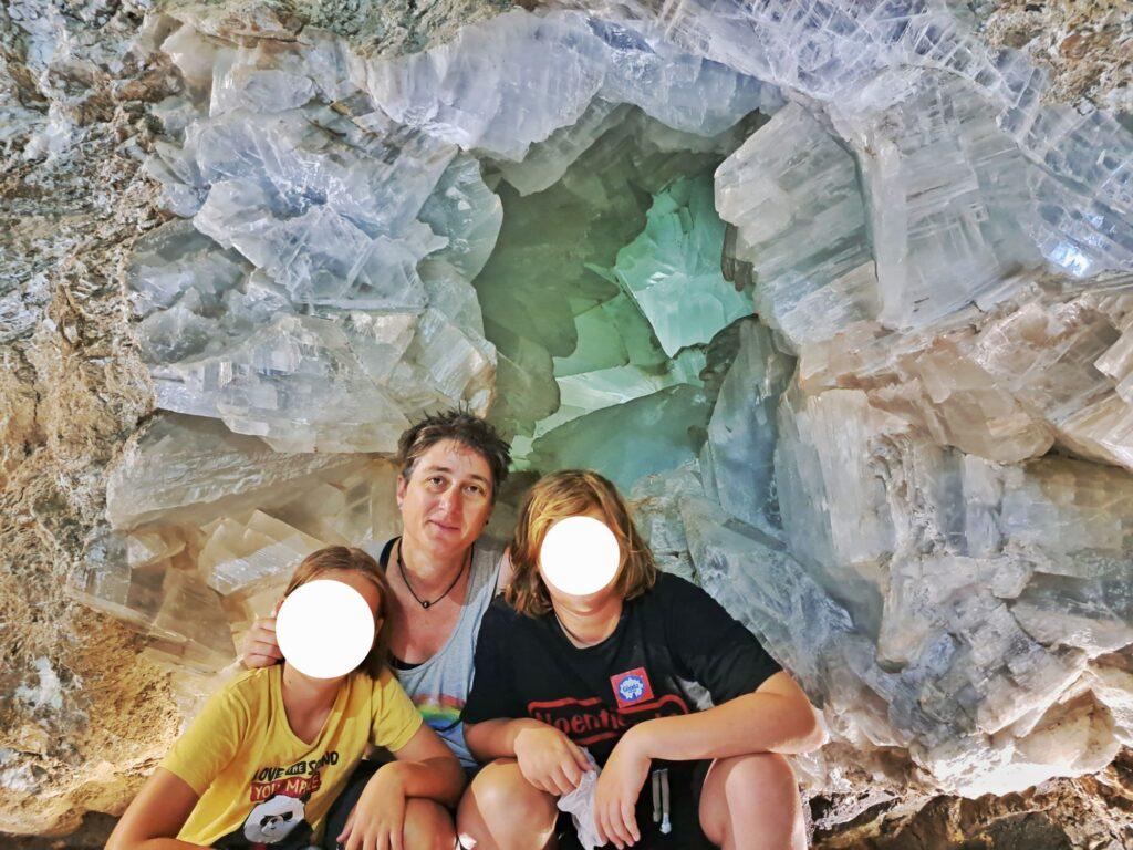 adult and 2 kids (white circles on faces) in front of enormous geode