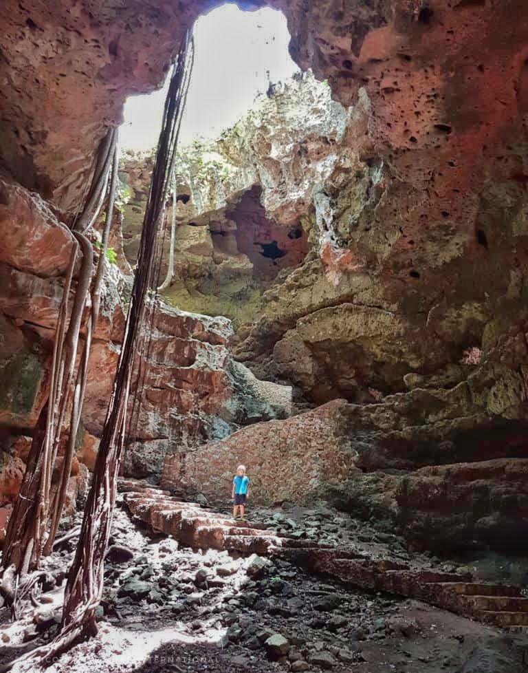 child in blue tshirt standing in an enormous cave with an opening above