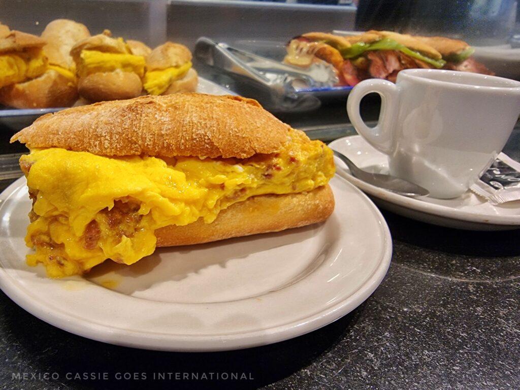 spanish tortilla in bread roll next to a cup of coffee