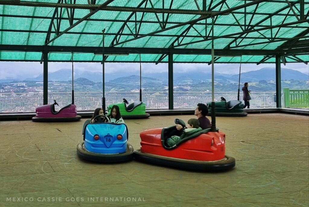 2 dodgems, 1 red, 1 blue, green roof, view over hills behind