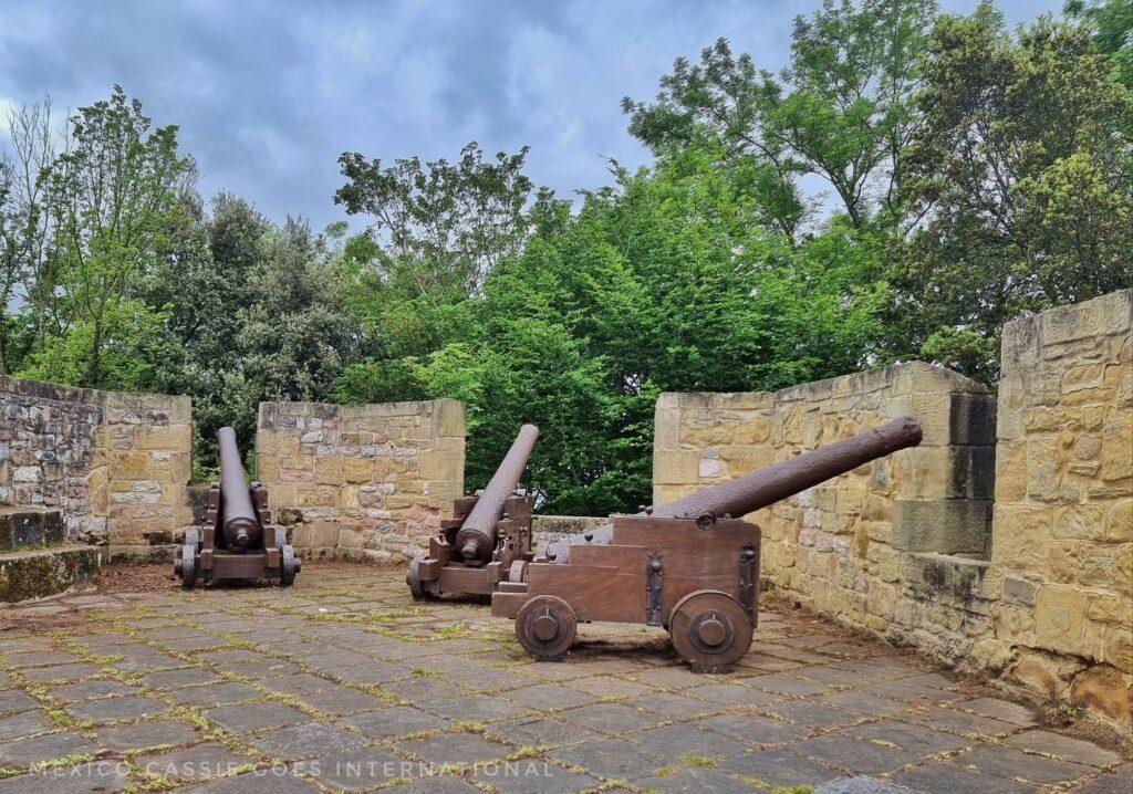 3 old cannons pointing out over a low wall - trees behind