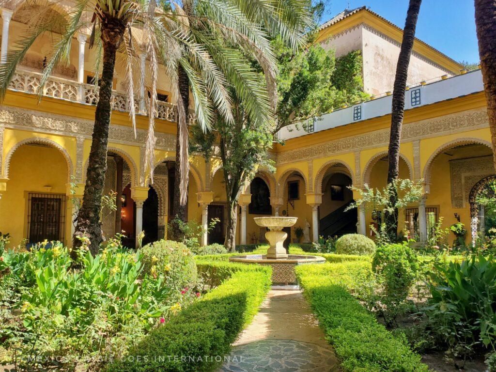 beautiful old courtyard with trees, bushes and yellow arches