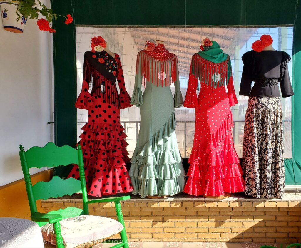 4 flamenco dresses on mannequins, green chair in front to one side