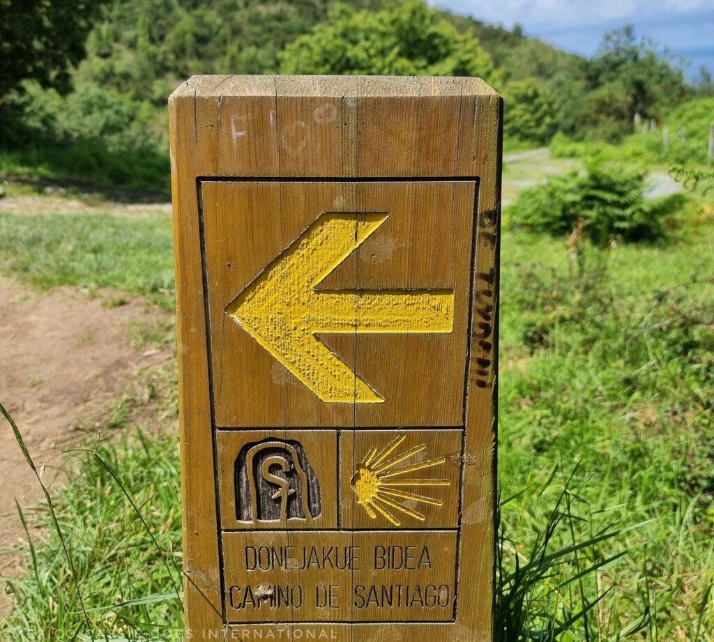 wooden sign post with yellow arrow and small camino conch in yellow