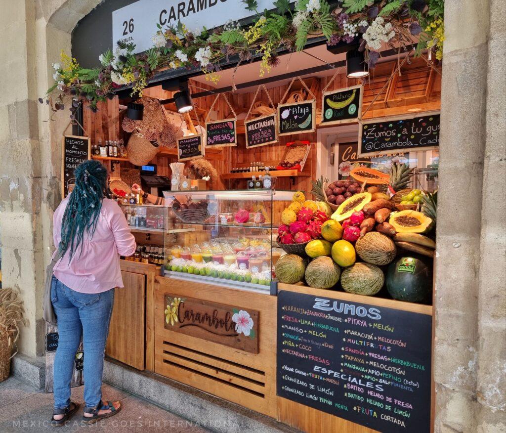 woman with blue hair and pink shirt making a purchase at a colourful fruit market stand