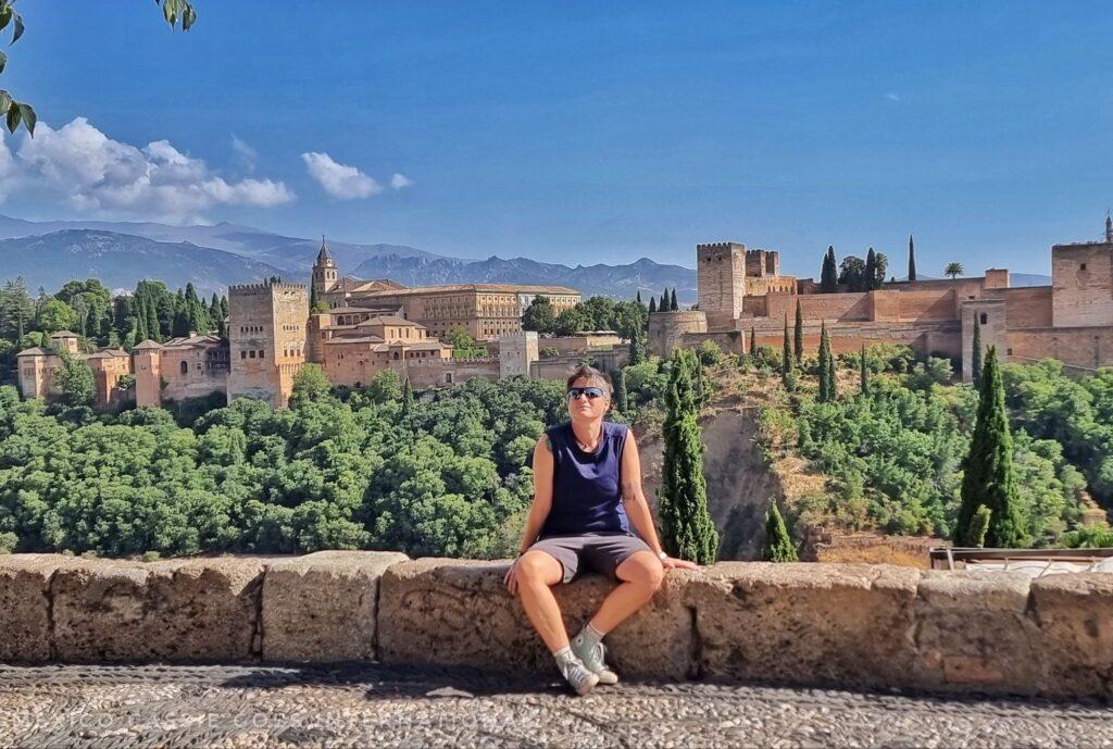 mexicocassie in a blue tshirt sitting on a wall in front of a view of the alhambra