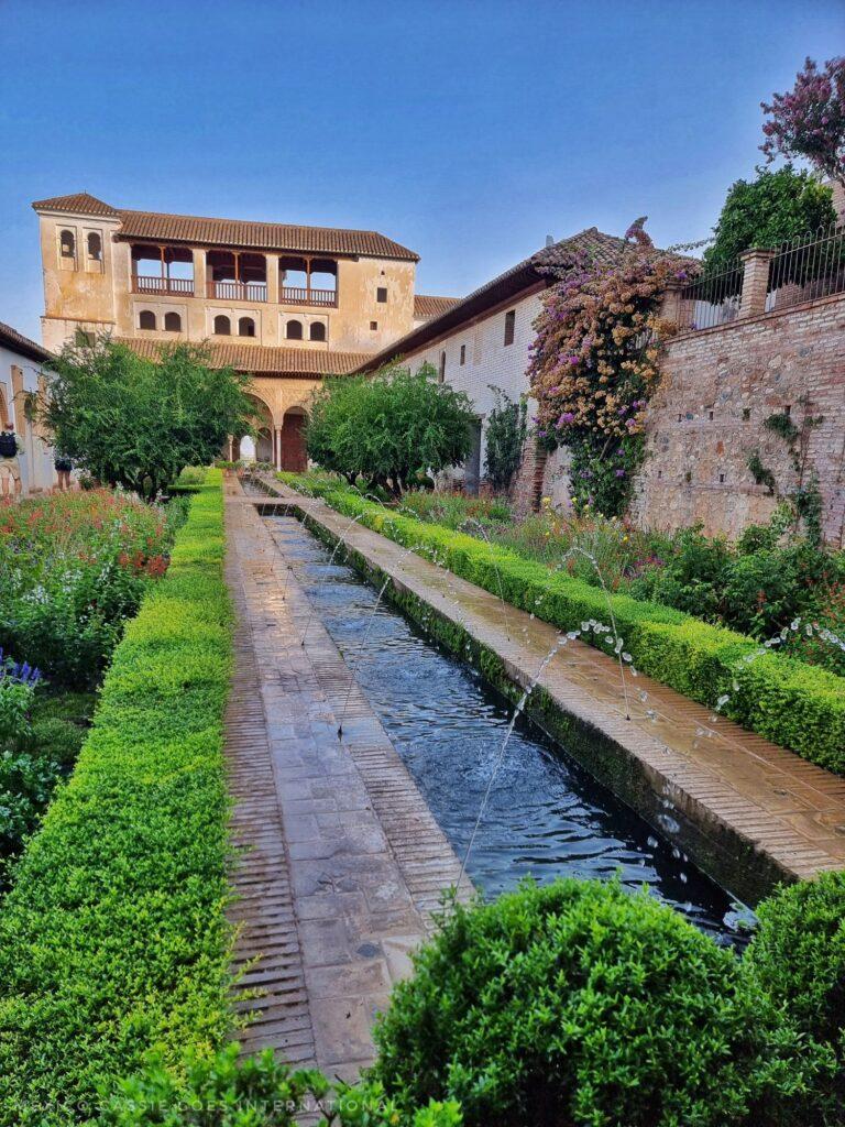 stream of water with small fountains, green bushes and lovely building at the far end