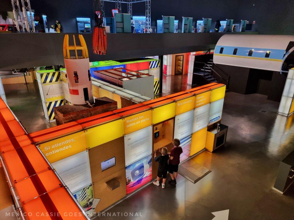 2 kids about  to enter an exhibit in a science museum, fairly dark room, yellow, orange and white lit blocks