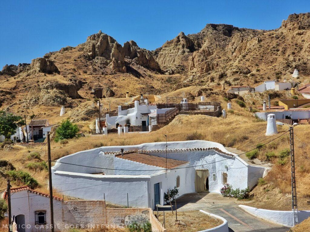 white house built into the curve of the land, other hoses and hills around