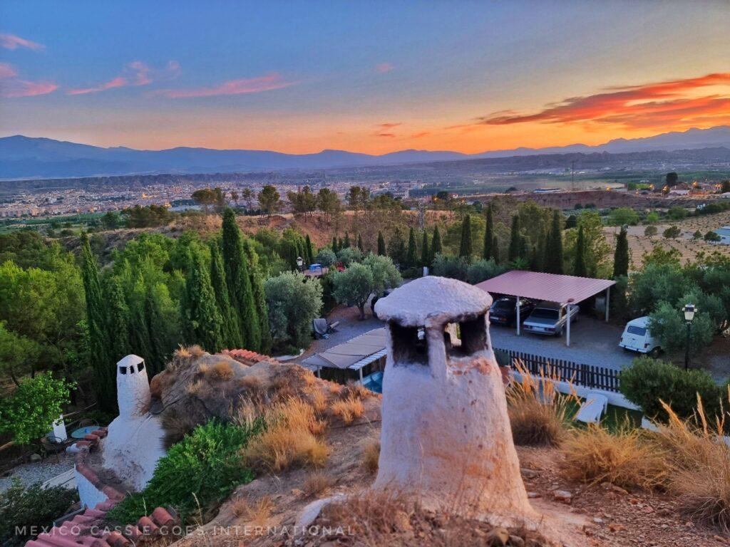 sun setting over guadix, white chimney and trees in foreground