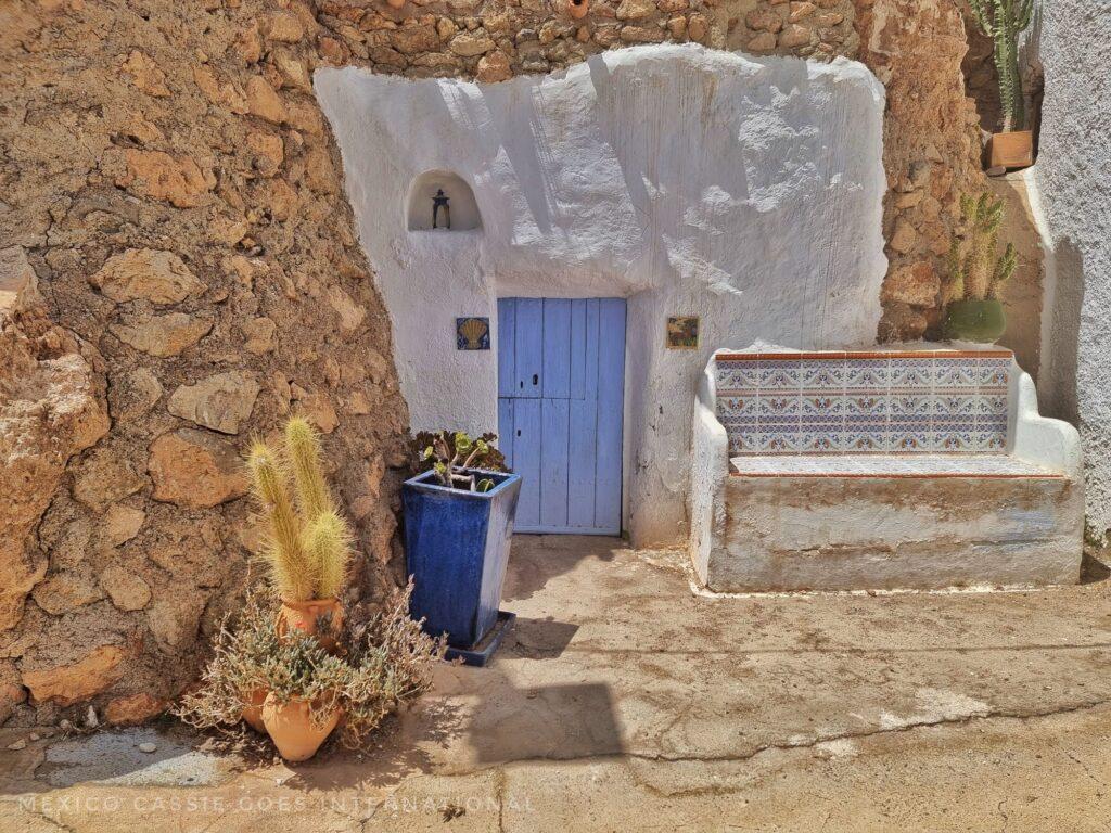 small light blue door with white plaster around it, bench outside, stone wall