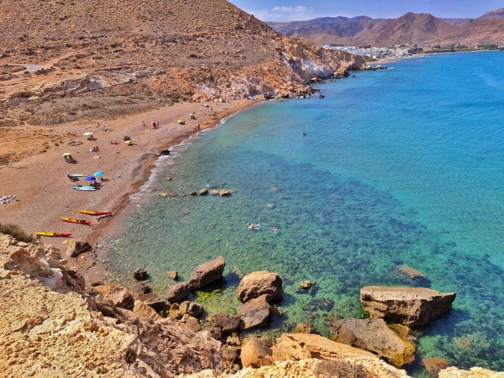 looking down over gentle bay with gorgeous blue water, people on beach