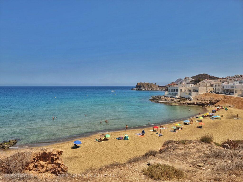 beach, sand, calm, blue water, people with umbrellas on the beach