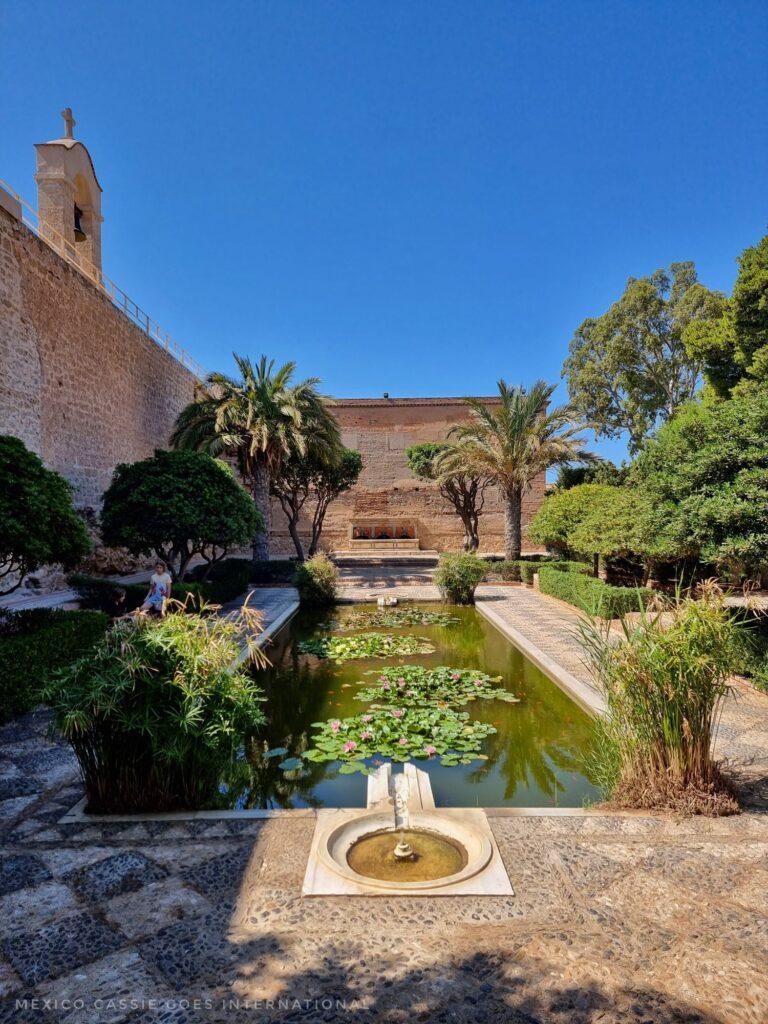 looking over the Alcazaba gardens - a long green pond with lily pads, fountain at front and building at far end