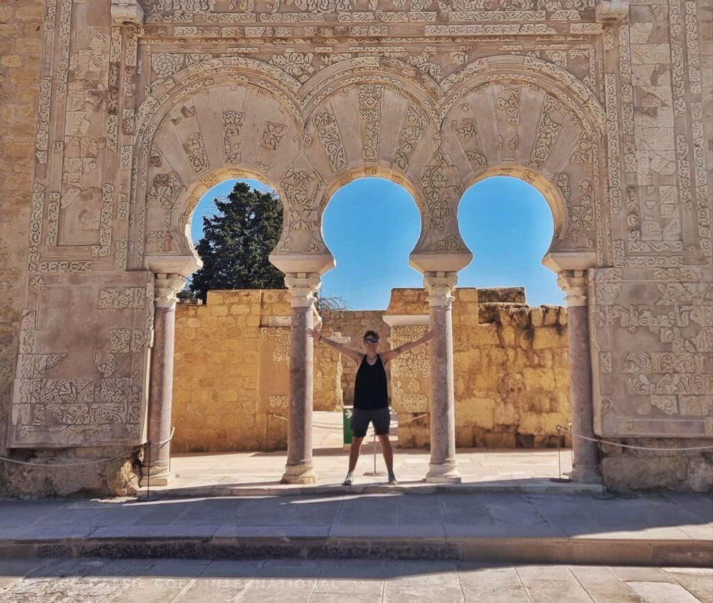 person in black standing in centre of 3 white arches, intricate carving 