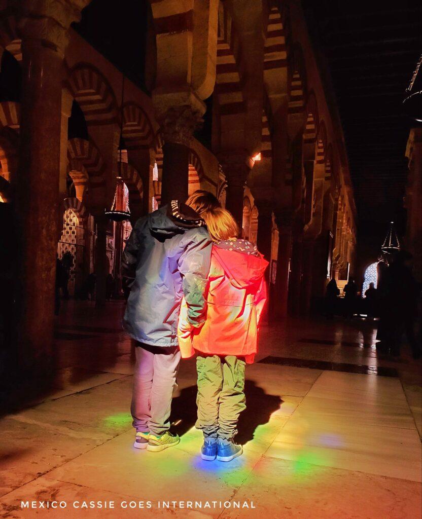 two kids standing in a dark church with rainbow refracted light on them