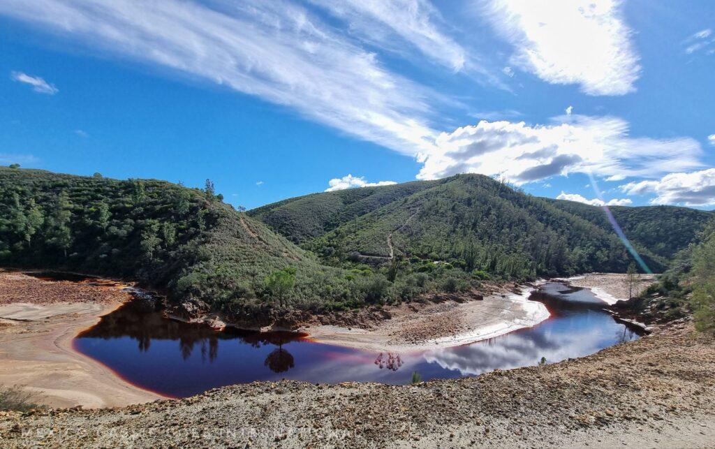 red river on a sunny day- trees behind, blue sky and reflections in the red water