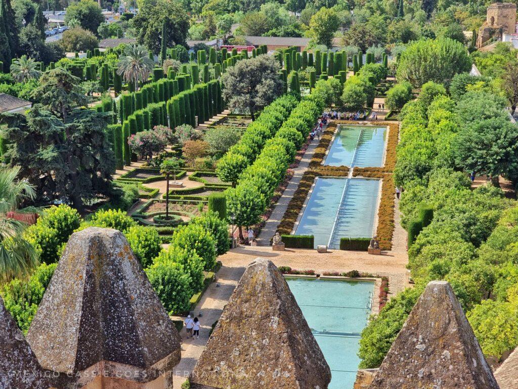 view over gorgeous gardens of the alcazar - long blue ponds (like swimming pools), trees - shot taken with points of defensive wall in foreground