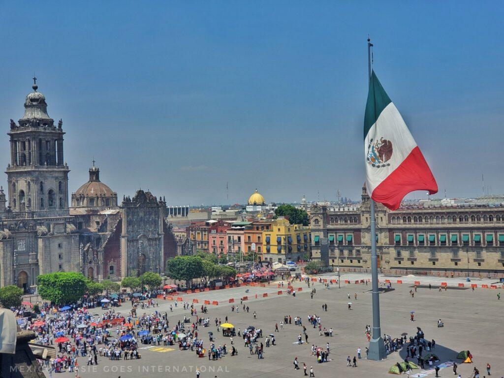 looking down onto mexico city's zocalo - small crowd of people, mexican flag flying, blue sky