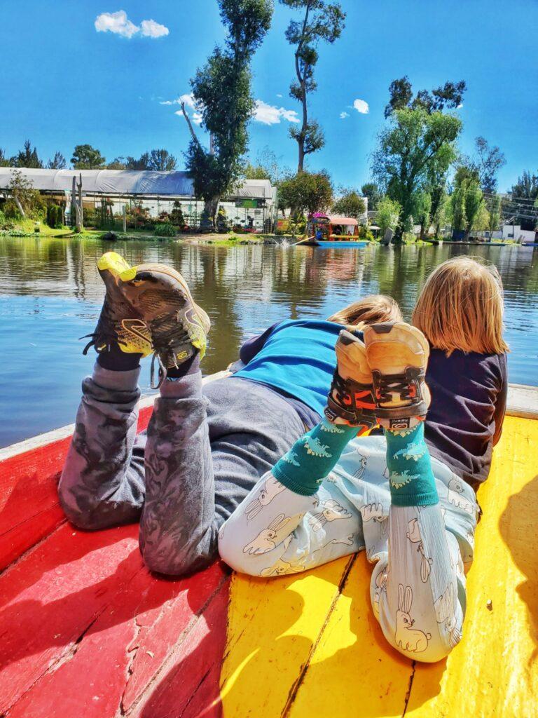 2 kids lying (facing away from camera) on a red/yellow barge on calm water