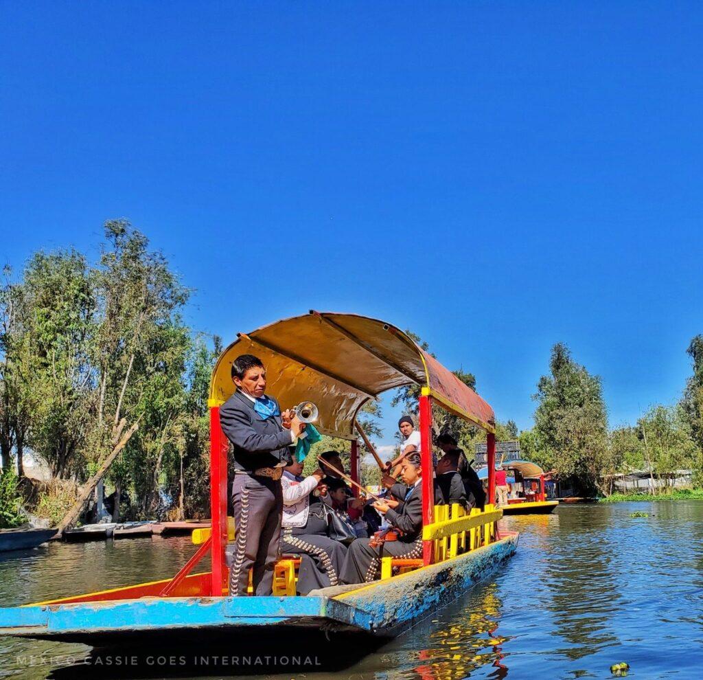 mariachi musicians on a red and yellow boat on canal