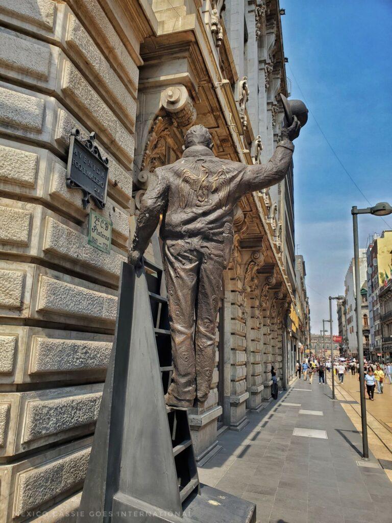 pedestrianised road with iron sculpture of a man on a ladder waving his hat