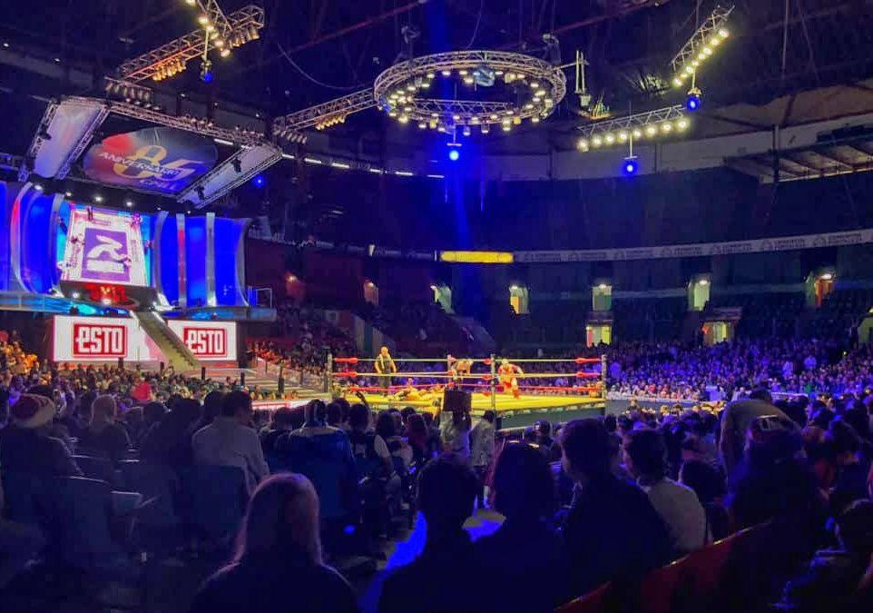 lucha libre stadium with a fight taking place on a lit ring in the distance, ring of lights above the stage