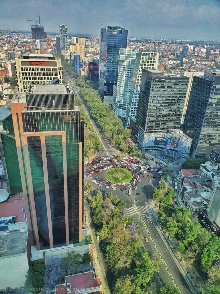 view looking down over CDMX's Paseo de Reforma, you can see tall buildings, tree lined streets and a busy roundabout