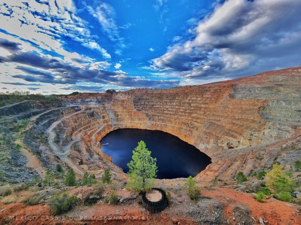 deep mining area with water in middle (deep water). Pine tree in front and blue skies with clouds