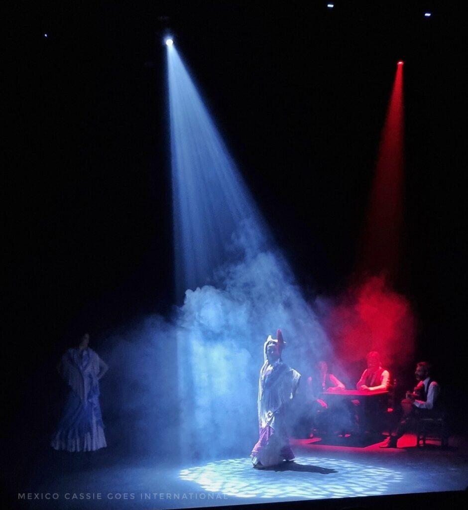 dark stage, spotlight on a flamenco dancer, guitarist and singers in dark behind. 